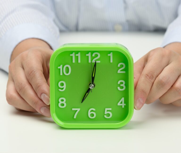 Woman's hand holds a green square alarm clock, the clock shows seven in the morning.